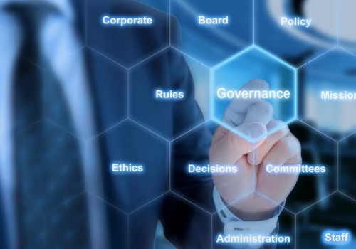 Businessman in blue suit in front of office background clicking tile with the word governance in hexagon grid
